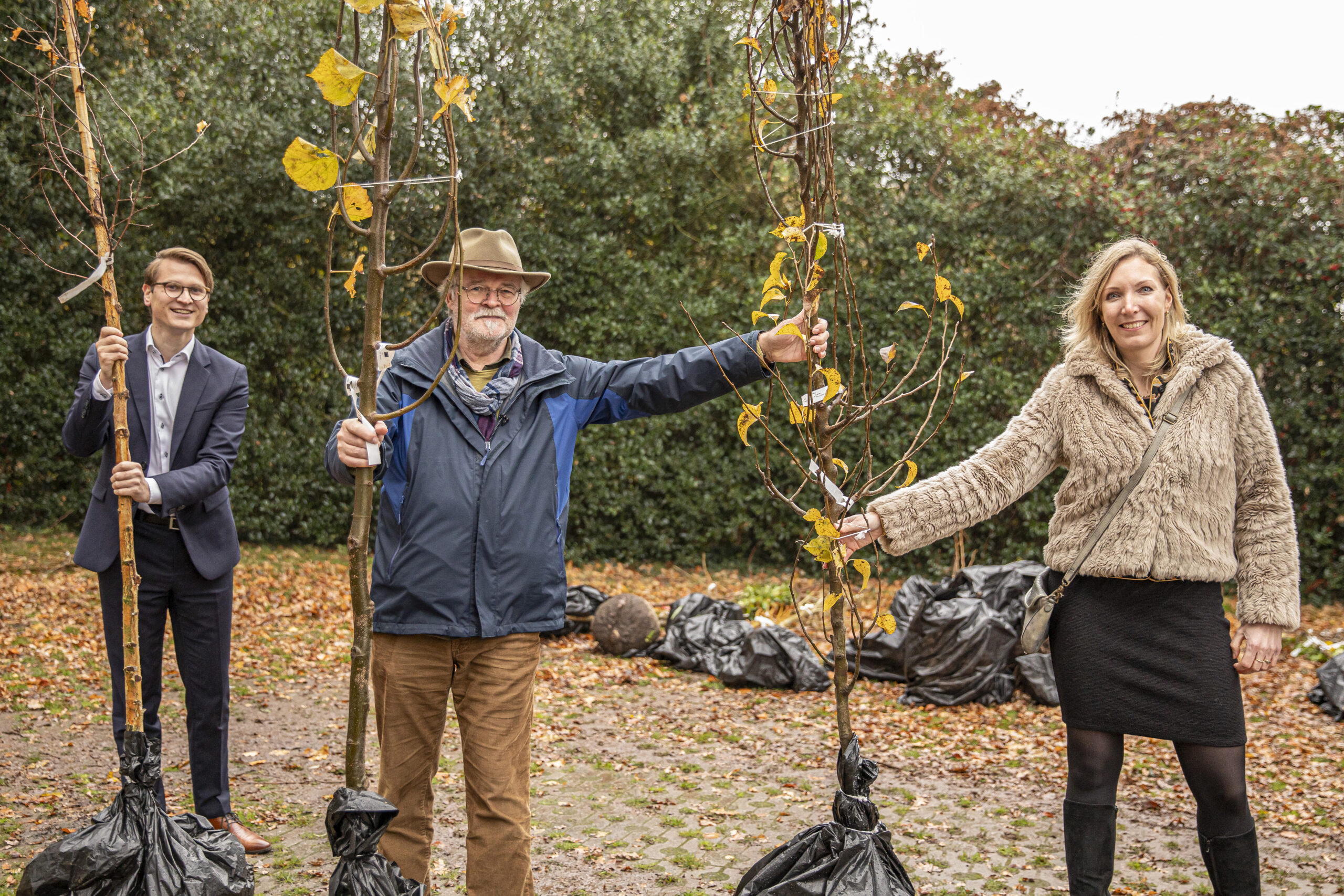 Twee mannen en een vrouw poseren met een boom die wordt geplant.