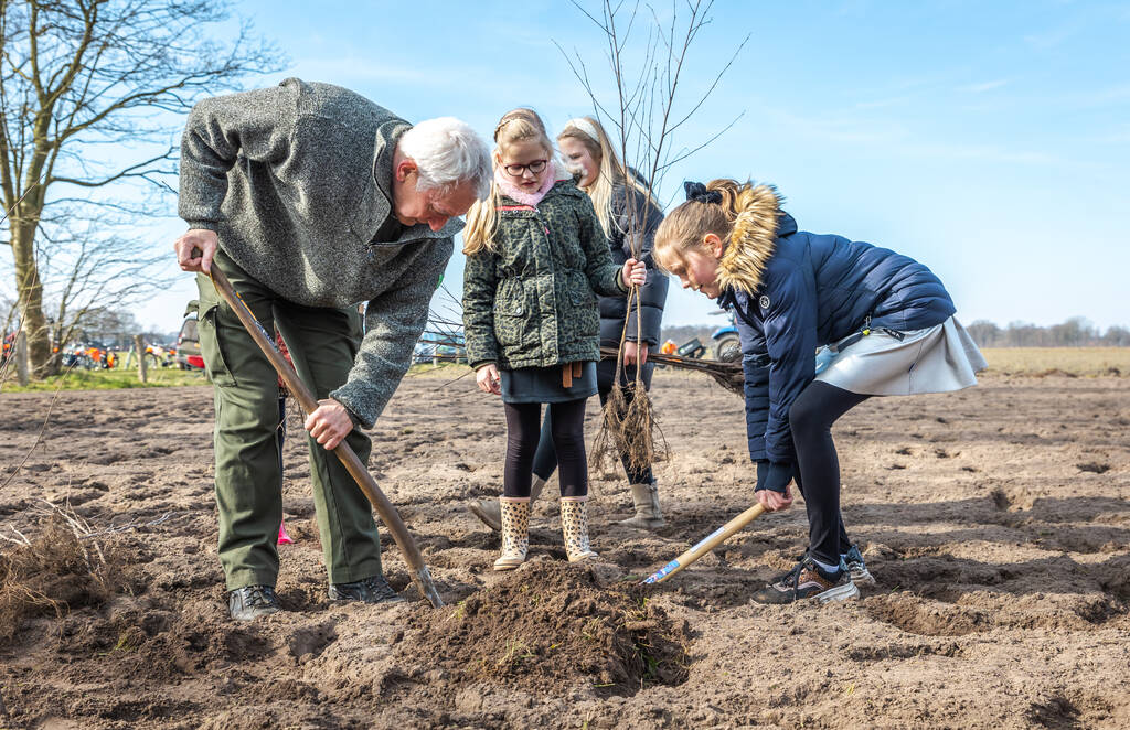 Een groepje van mensen plant gezamenlijk een boom. Ze steken de schop net in de grond.
