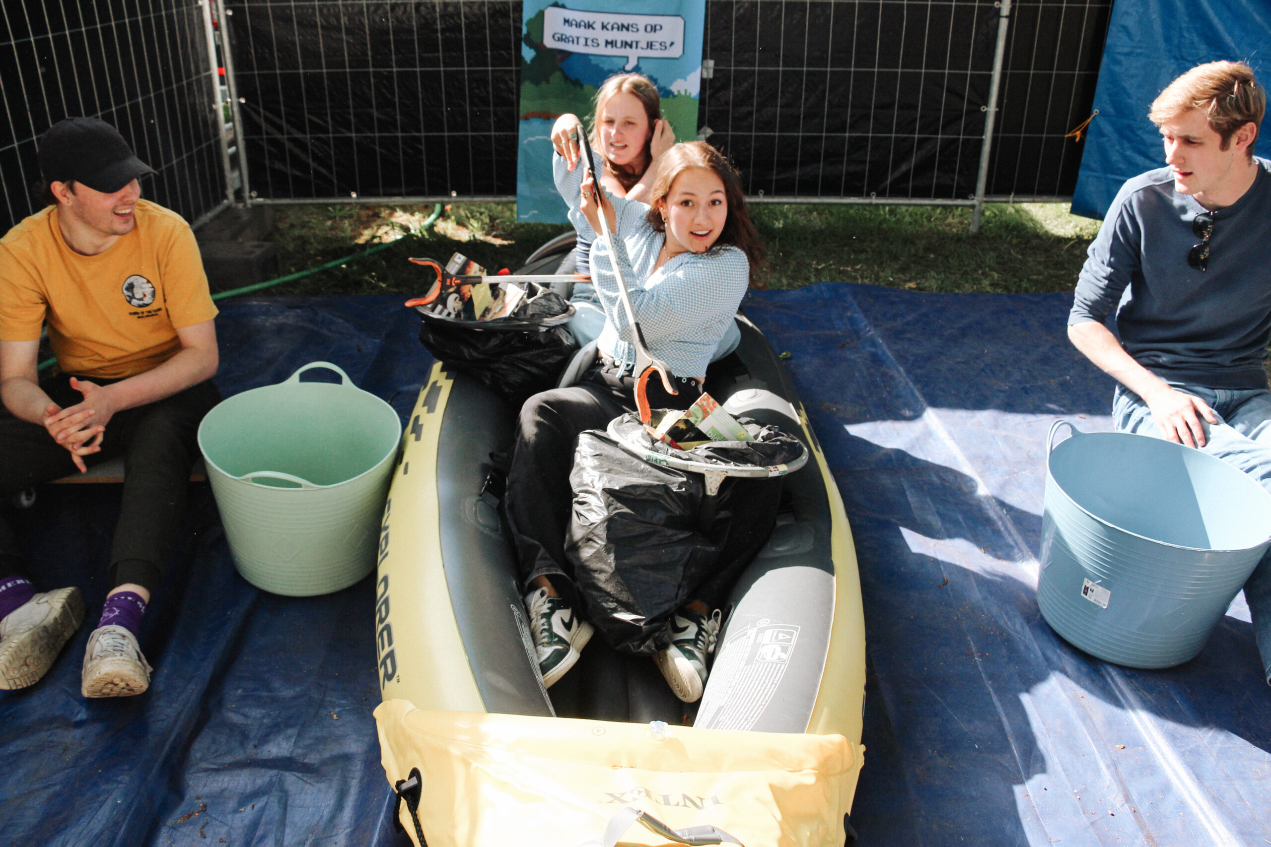 Twee jonge deelnemers roeien in een kano op het droge terwijl ze afval prikken