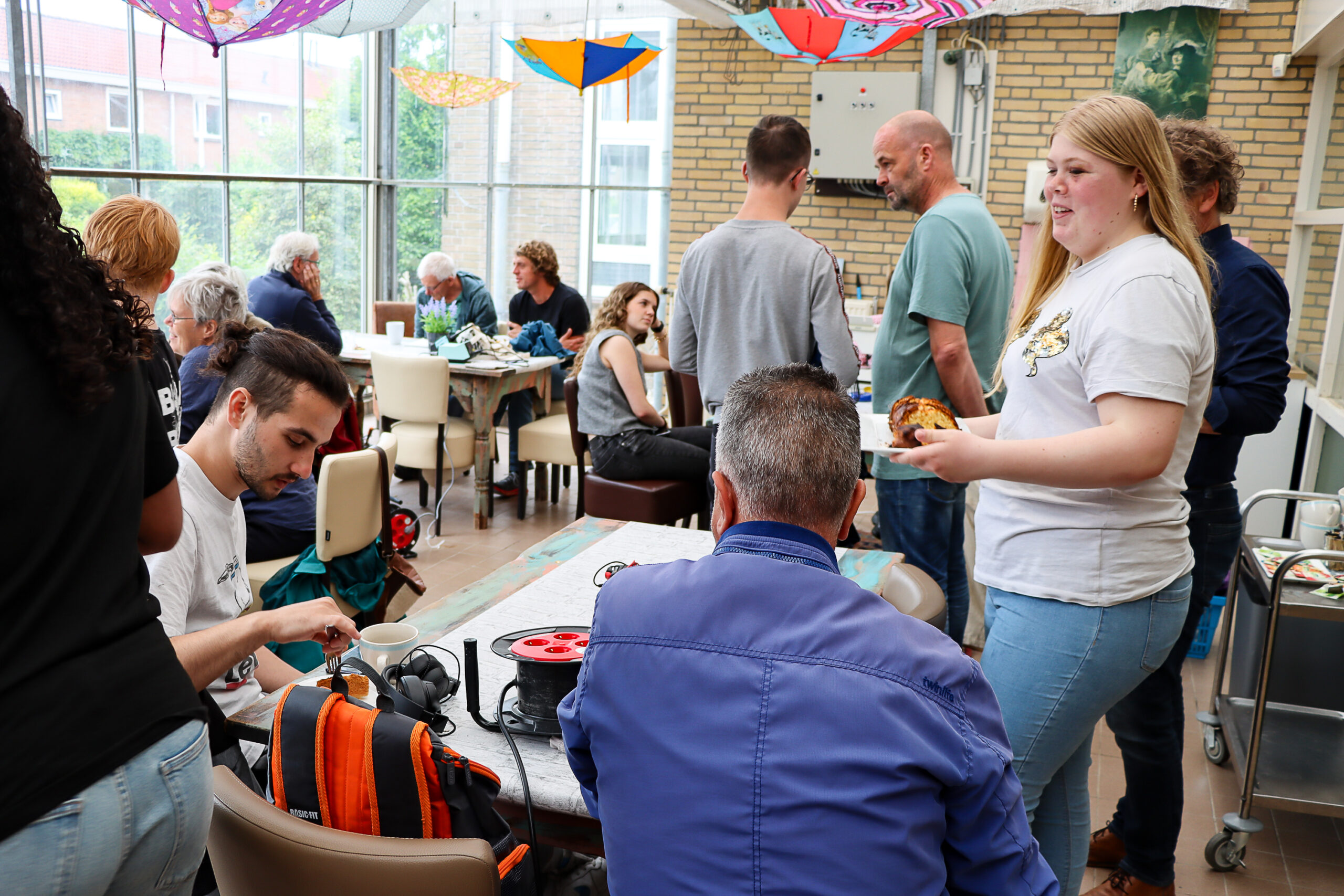 Mensen samen in een feestelijk versierde ruimte voor het eerste Repair Café van Arbeidstrainingscentrum TIB. 